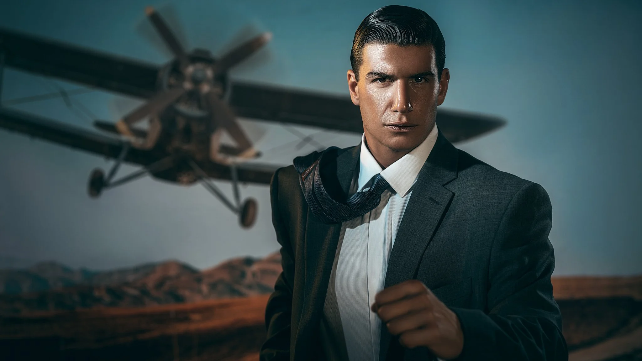 Cinematic portrait of a man in a dark suit in front of a vintage propeller aircraft